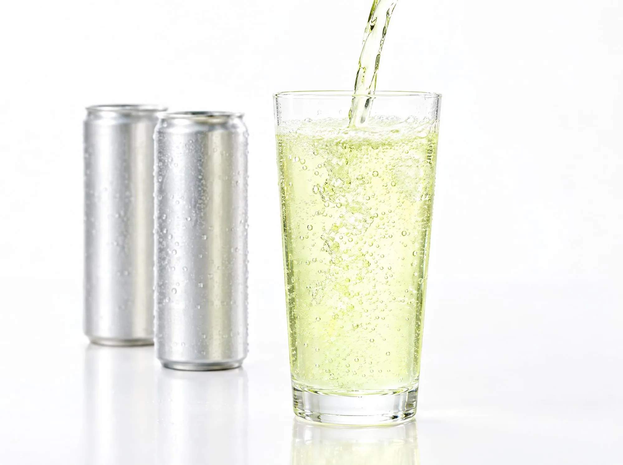 A pale sparkling drink being poured into a glass in front of two plain aluminium cans